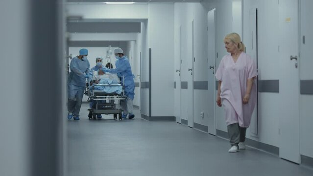 Doctors and nurses run and push gurney with seriously injured patient to operation room. Professional medical personnel save human life in emergency department. Medical facility hallway. Slow motion.