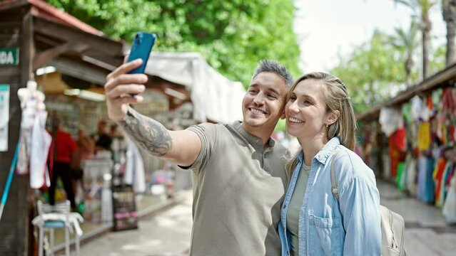 Man and woman couple smiling confident make selfie by smartphone at street market