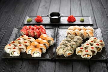 Assorted sushi rolls set served on black stone slate on dark background with ginger and wasabi