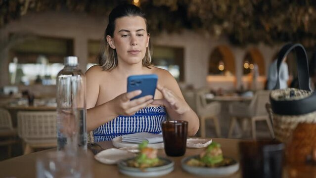 Young hispanic woman taking pictures to the food sitting on the table at the restaurant