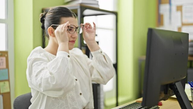 Young beautiful hispanic woman working taking glasses off at the office