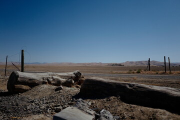 Desert road with logs and fence and blue sky.