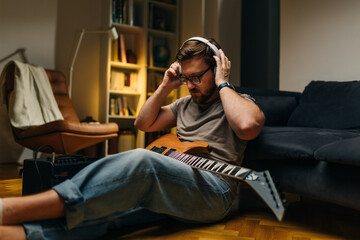 Musician sitting on the floor at home with an electric guitar and putting on headphones.