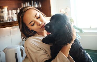 Love, hug and woman with a dog in home kitchen to relax and play with animal. Pet owner, happiness and asian person playing with companion, care and wellness or friendship in cozy apartment