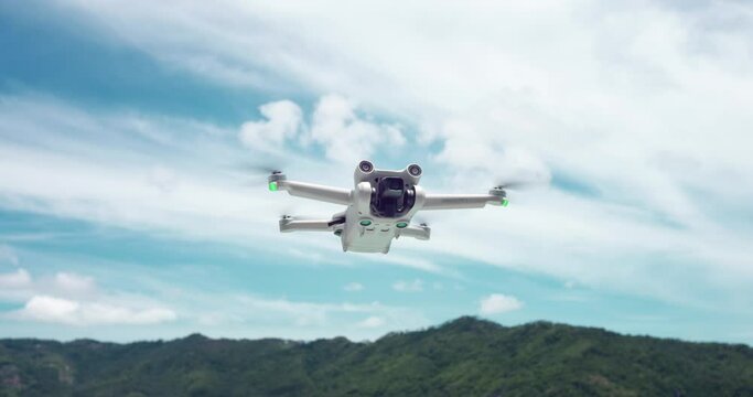 Drone aircraft flying in slow motion. Drone copter hovered in the air on cloudy sky and mountains background. Travel blogger making aerial view videos and photos with drone or copter while traveling