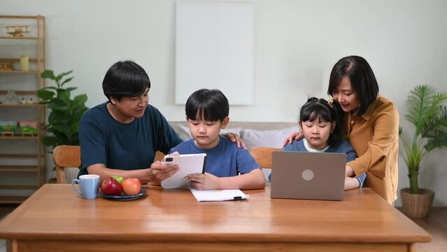 Parents assisting children doing homework at desk. asian son is doing a homework on the notebook