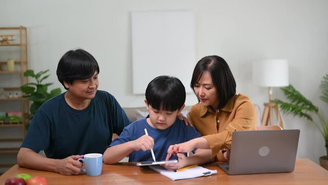 Parents assisting children doing homework at desk. asian son is doing a homework on the notebook