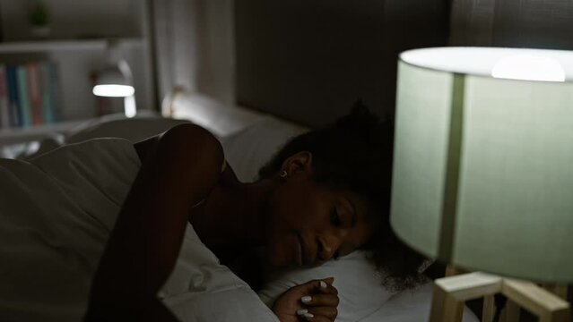African american woman lying on bed turning off lamp to sleep at bedroom