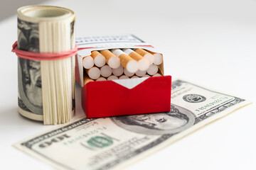 Pack of cigarettes with one hundred dollar bills on a blue background. Smoking costs