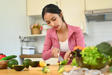 Obraz na płótnie Canvas Beautiful woman cutting avocado on chopping wood board, making vegetables salad in kitchen. Dieting and Healthy lifestyle concept