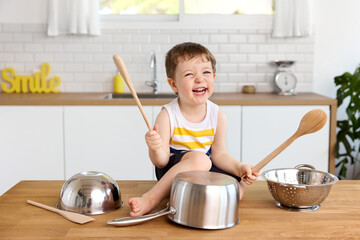 Happy toddler playing drums with pots and pans on kitchen table