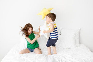 Wild siblings having a pillow fight on white bed