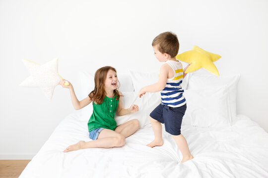 Happy siblings having a pillow fight on white bed