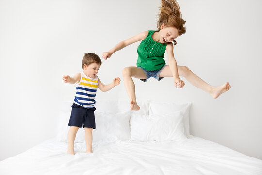 Brother and sister wildly bouncing on white bed