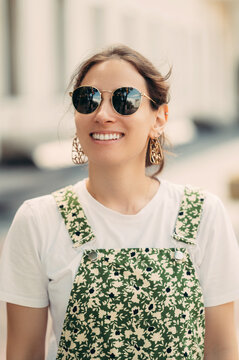 Vertical outdoors close up portrait of a wide smiling woman wearing sunglasses.