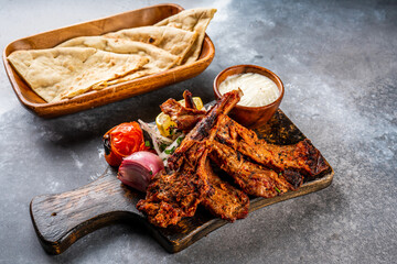 Mutton Champ or lamb chop bbq grill with pita bread, nan, tandoori roti, raita, dip and salad, tomato onion and lemon served in wooden board top view on background spicy barbeque