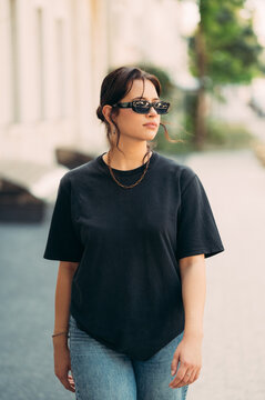 Vertical outdoors portrait of a serious young woman walking on the street with sunglasses on.