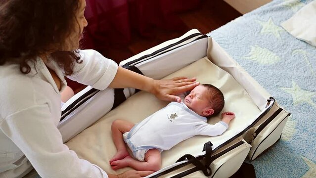 Overhead view of newborn baby sleeping in a transportable crib and his loving caring mother caressing him. Pregnancy. Childbearing. Childbirth. Maternity leave. People, early childhood and lifestyles