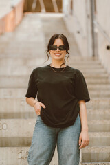 Obraz premium Vertical portrait of a young smiling woman wearing sunglasses while standing on some stairs.
