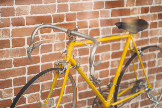 Close up crop shot of a nice yellow bicycle leaning on a brick wall outdoors.
