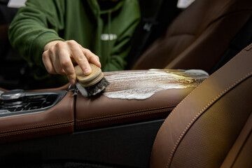 Closeup leather car interior cleaning with foam detergent and brush - obrazy, fototapety, plakaty