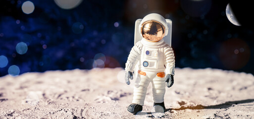 immagine primo piano statuina di astronauta nella tuta spaziale sulla superficie di una luna aliena, spazio scuro e pianeti sullo sfondo
