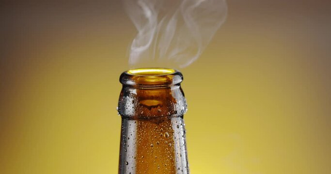 Beer bottle is opened with a bottle opener, the cap flies into the background, and the condensation of beer gas rises up from the neck. 