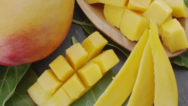 Ripe mango fruits with slices and mango leaves slowly move in the frame on a gray stone table. Nice fruit background for your projects. Macro video shooting.
