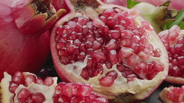 Ripe pomegranate fruits with slices and pomegranate tree leaves slowly move in the frame on a gray stone table. Nice fruit background for your projects. Macro video shooting.