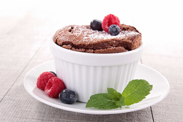 Decadent Chocolate Soufflé Topped with Fresh Berries and a Dusting of Powdered Sugar, Served in a White Ramekin on a Pristine White Plate, Perfectly Complemented by a Sprig of Mint