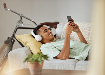 Headphones, phone video and man on a living room sofa happy and relax at home. Series, funny app and laughing with music and listening in a house lounge with web mobile streaming and couch with smile