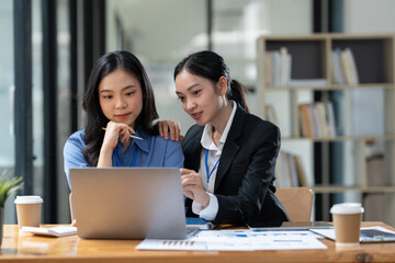 Two Asian businesswomen discuss investment project work and planning strategy Brainstorm together Find information online on iPad Laptop and tablet for making reports and summarizing business results