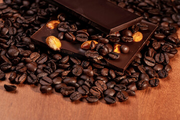 Coffee beans and dark chocolate with golden almonds on wooden background.