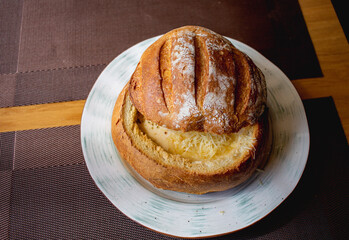 Cheese soup baked in a bread roll. Ruddy bread, light brown cut top, filled with cheese soup and served on a plate.