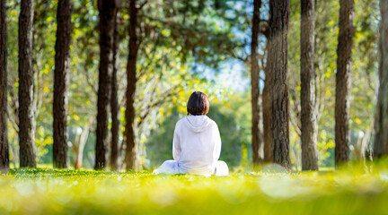 Woman relaxingly practicing meditation in the pine forest to attain happiness from inner peace...