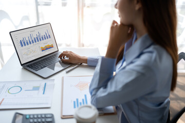 Asian businesswoman sitting and thinking analyze financial reports Business growth using laptop...