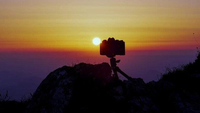 Time lapse of colorful sunset silhouetting camera on tripod 