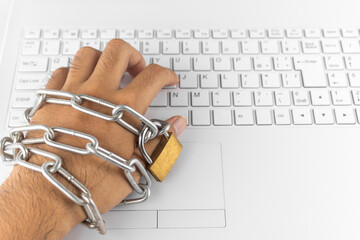 鎖の巻かれた手とノートパソコンのキーボード。依存症のイメージ