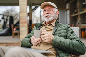 One senior man sit outdoor in autumn day hold cup of coffee or tea