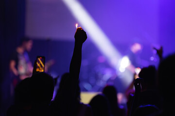 A man in the crowd pulls his hand with a lighter up at a concert