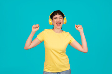 Portrait of a smiling and dancing woman with yellow headphones  in yellow t-shirt on blue background. do what you like