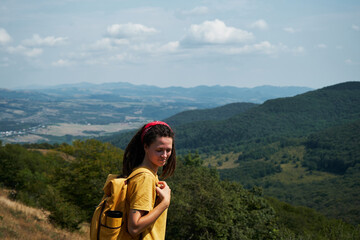 Concept of tourism and travel. A young woman with dreadlocks and a yellow backpack stands on top of a mountain and enjoys the views of nature. Algeti National Park, Georgia.