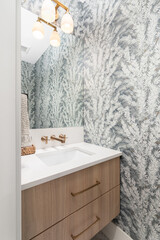 A bathroom with floral wallpaper, a floating wood vanity cabinet, marble countertop, and gold light...