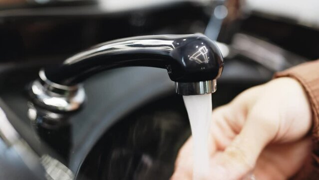 A man without a face washes his hands in a black sink. Close-up. Concept of hygiene, cleanliness.
