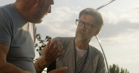 Close up shot of doctor sitting with patient on bench and examining his shoulder. Elderly man...