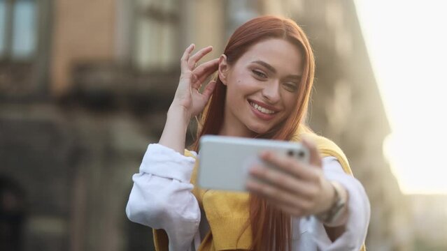 Portrait of young red hair woman grimacing taking selfie photograph saving great memories on smartphone mobile phone at sunny city centre Pretty girl create content for social media outdoors