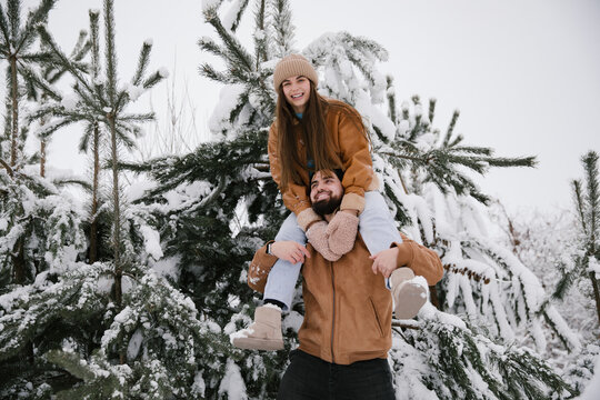 A woman sitting on the shoulders of a man in winter in the snow among snow-covered pines. A couple have fun in a snowy forest in winter.