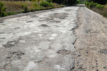 Bad road, cracked asphalt with potholes and big holes. Potholes on the road with stones on the...