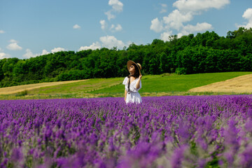 Beautiful lady in a lavender flower field on a summer day. A beautiful woman enjoys a blooming lavender field. Portrait of a young woman in a hat with a bouquet of lavender. 4K, UHD