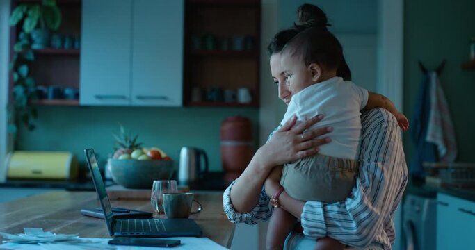 Laptop, remote work or finance with a mother and baby in a home in the evening for overtime. Computer, family and business woman multitasking in the kitchen with her infant child as a single parent